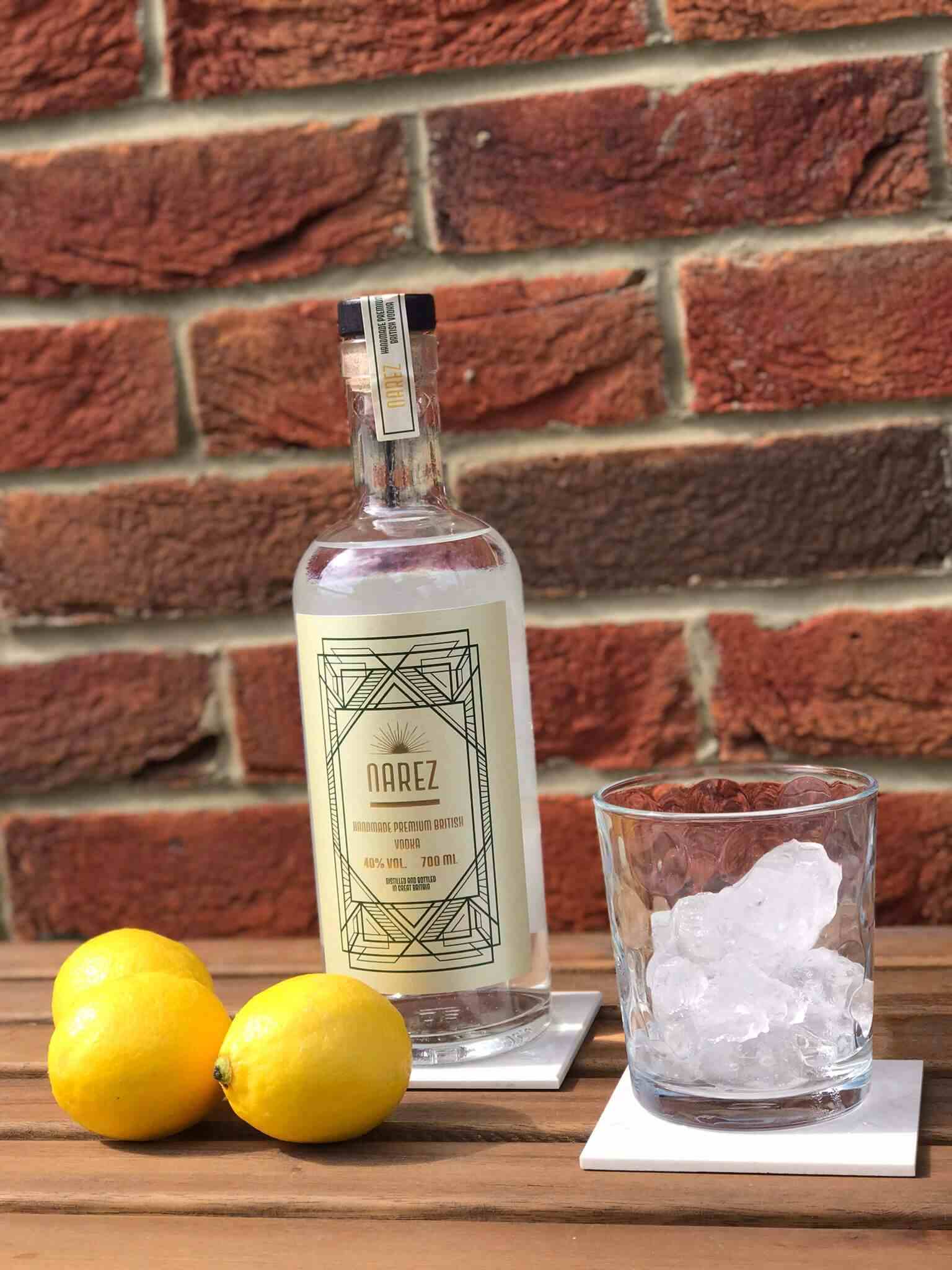 Narez Organic Vodka 70cl bottle with lemons and ice-filled glass on wooden table against brick wall.