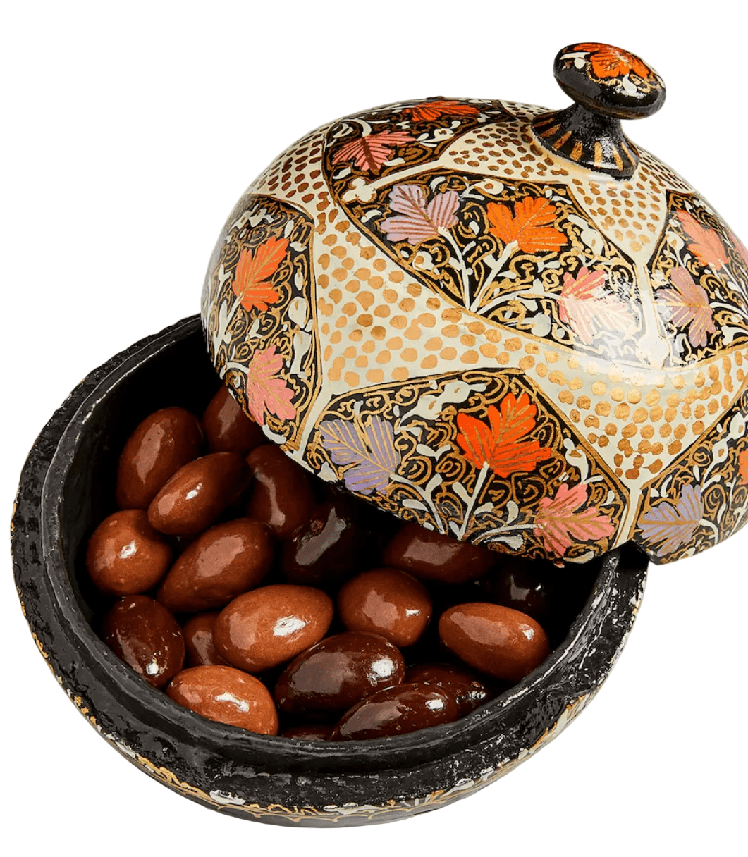 Decorative container with floral patterns filled with almonds on a marble surface
