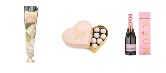 This luxurious Valentine's Day gift set features a single elegant long-stemmed pink rose wrapped in clear cellophane with a delicate white pearl-like ribbon cuff at the base, an open heart-shaped pink Godiva box revealing white-dusted champagne truffles arranged neatly inside, and a full bottle of Moët & Chandon Rosé Impérial champagne with its signature soft pink label and festive branding, all arranged side by side in a cohesive romantic pink color scheme perfect for expressing love and celebration.