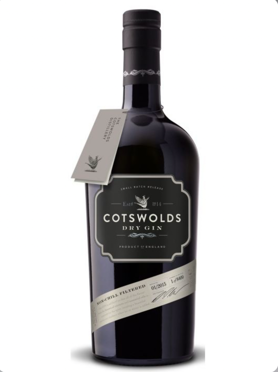 Dark purple-black glass bottle of Cotswolds Dry Gin (70cl), filled with clear gin. The bottle has a black cap and a matte black label with a cream framed panel in the center: "COTSWOLDS" in large white capitals at the top, "DRY GIN" below, a small white pheasant illustration, "Est. 2014" with a bird emblem, and "SMALL BATCH RELEASE" in smaller text. A diagonal silver foil band wraps around the bottle with "NON-CHILL FILTERED", "01/2015", batch number "1 of 8400", and a handwritten-style signature.