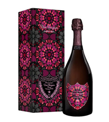 A bottle of Dom Pérignon Grand Cru Champagne next to its matching decorative gift box, both featuring a vibrant magenta, pink, and purple mandala pattern on a black background.