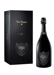 A bottle of Dom Perignon P2 Champagne next to its black presentation box, both featuring gold lettering and the classic shield logo, set against a clean white background with a subtle reflection.