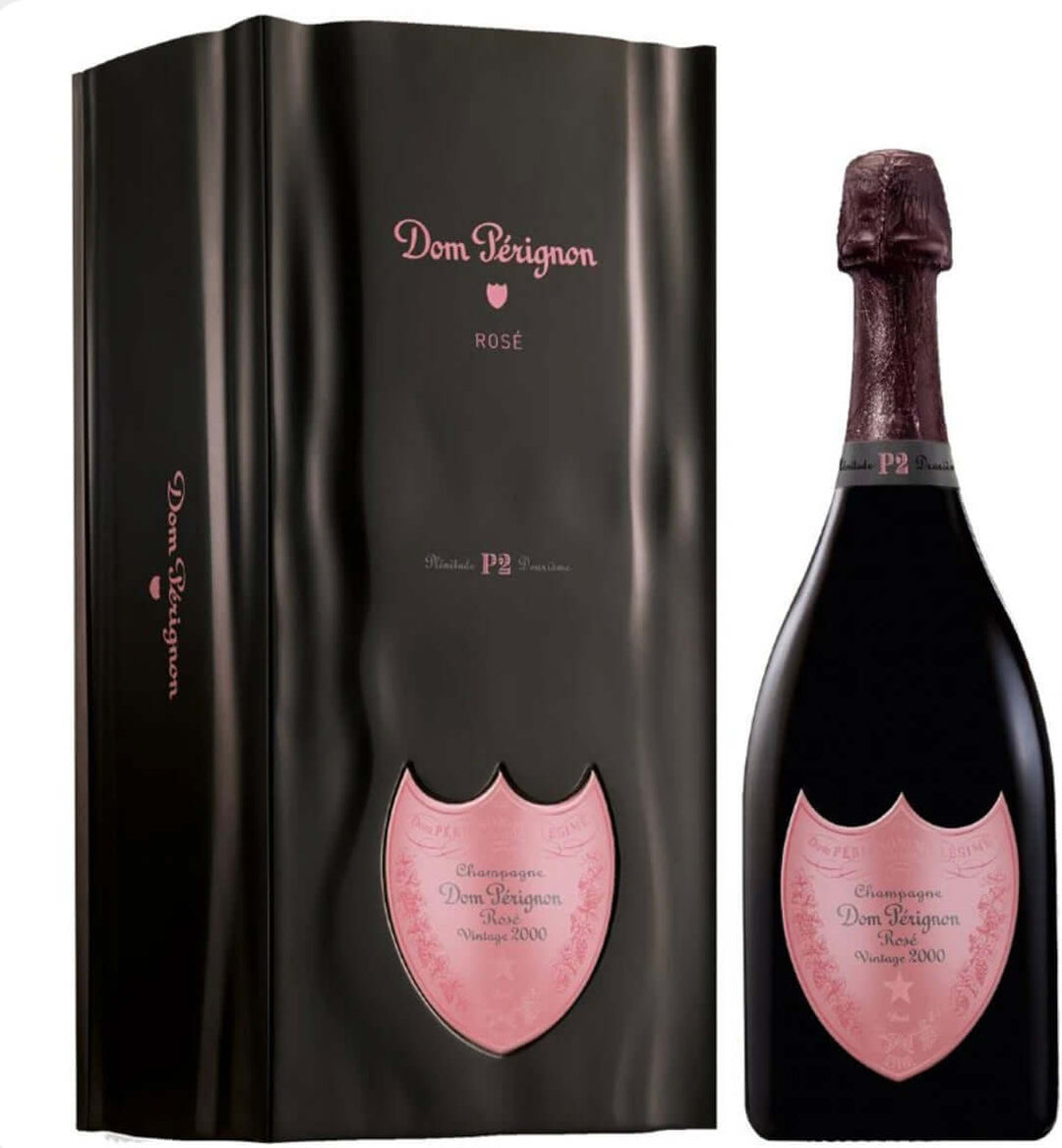 Black wavy gift box with pink accents and Dom Pérignon Rosé Plénitude P2 Vintage 2000 labeling next to the dark bottle of Dom Pérignon Rosé 2000 P2 Champagne, featuring a deep burgundy foil wrapper, pink shield label with vintage details, and 'P2' neck band, displayed against a plain background.