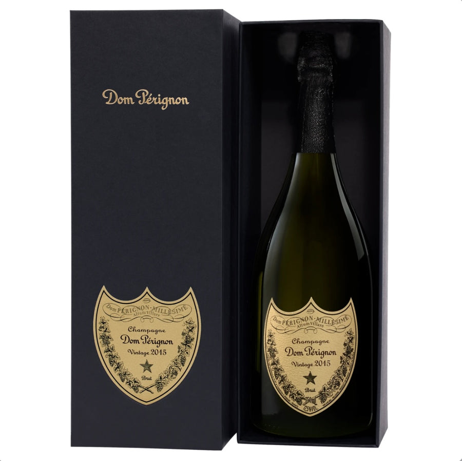 Open black gift box of Dom Pérignon Vintage 2015 Champagne 75cl with gold “Dom Pérignon” scripting on the lid, revealing the green bottle inside featuring a classic gold shield label with ornate detailing, “Champagne Dom Pérignon Vintage 2015 Brut” text, and a star emblem.