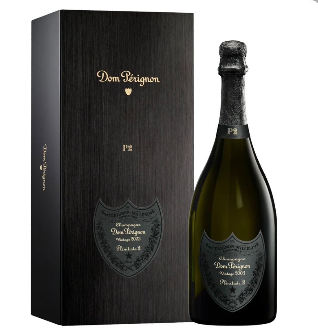 Dom Pérignon Plénitude 2 P2 Vintage 2003 Champagne bottle next to a sleek black gift box with gold “Dom Pérignon” and “P2” lettering, showcasing the bottle’s dark label with “Vintage 2003 Plénitude 2” details.