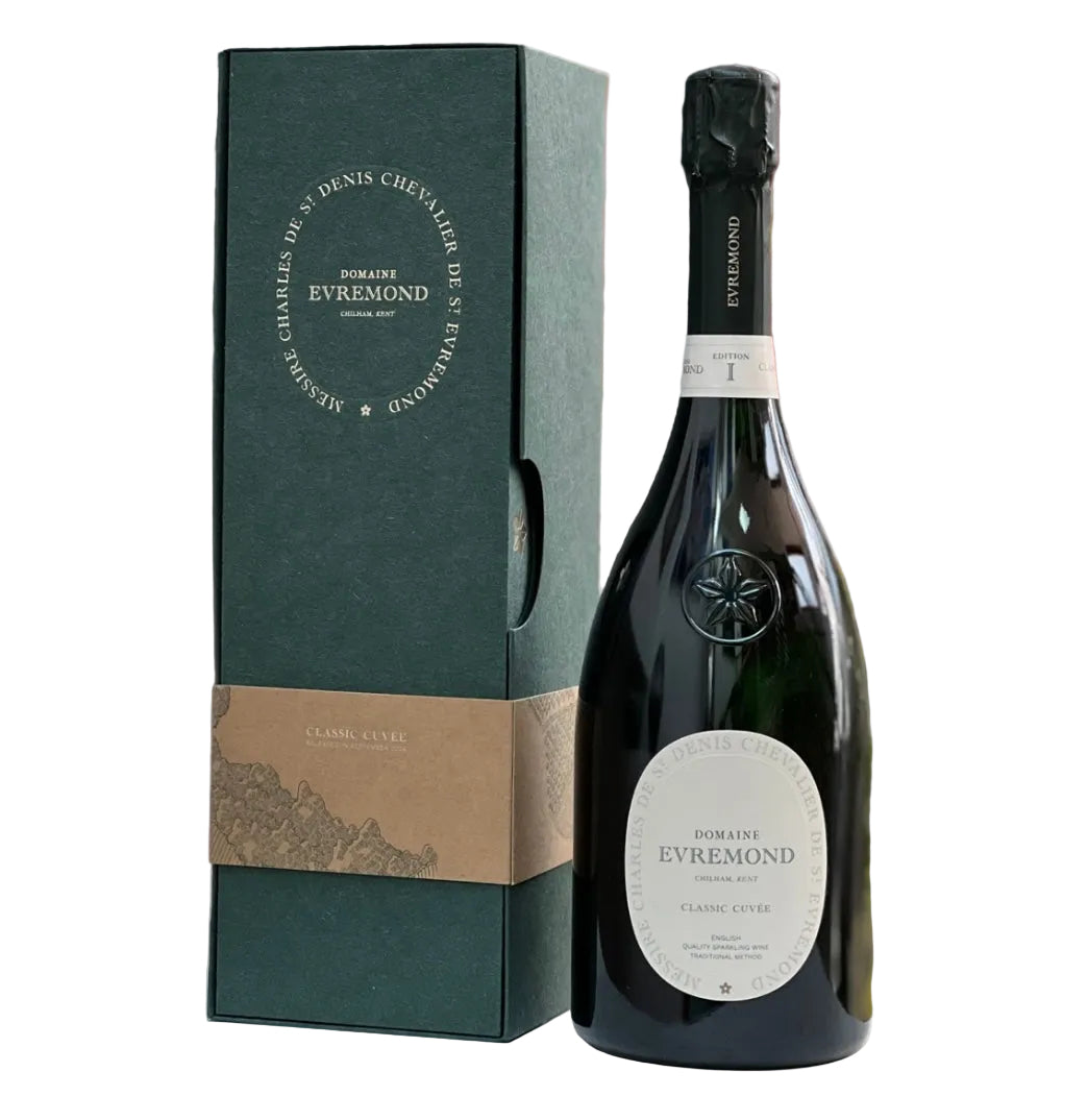 Dark green gift box with gold-embossed circular text "CHARLES DE ST DENIS CHEVALIER DE ST EVREMOND" and "DOMAINE EVREMOND CHILHAM KENT" around the edges, paired with a dark green foil-capped black glass bottle of Domaine Evremond Classic Cuvée Edition I. The bottle features an oval white label with arched text "CHARLES DE ST DENIS CHEVALIER DE ST EVREMOND" at the top, central "DOMAINE EVREMOND" and "CHILHAM, KENT" framing "CLASSIC CUVÉE", plus a small heraldic star emblem (cinquefoil). A kraft paper band ar