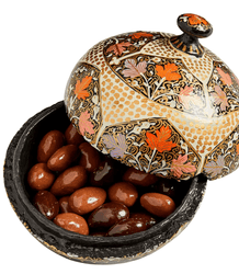 Decorative container with floral patterns filled with almonds on a marble surface