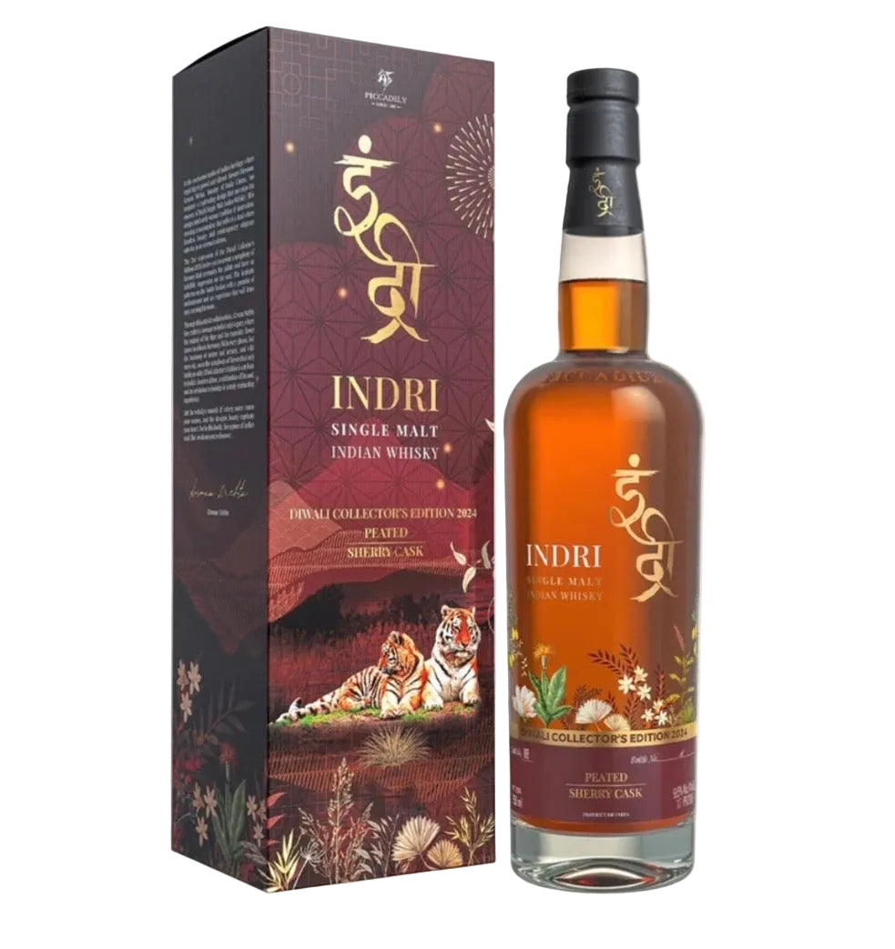 A bottle of Indri Single Malt Indian Whisky next to its matching retail box. The bottle contains amber-colored whisky and features a label with gold Devanagari script, white flowers, and botanical illustrations.
