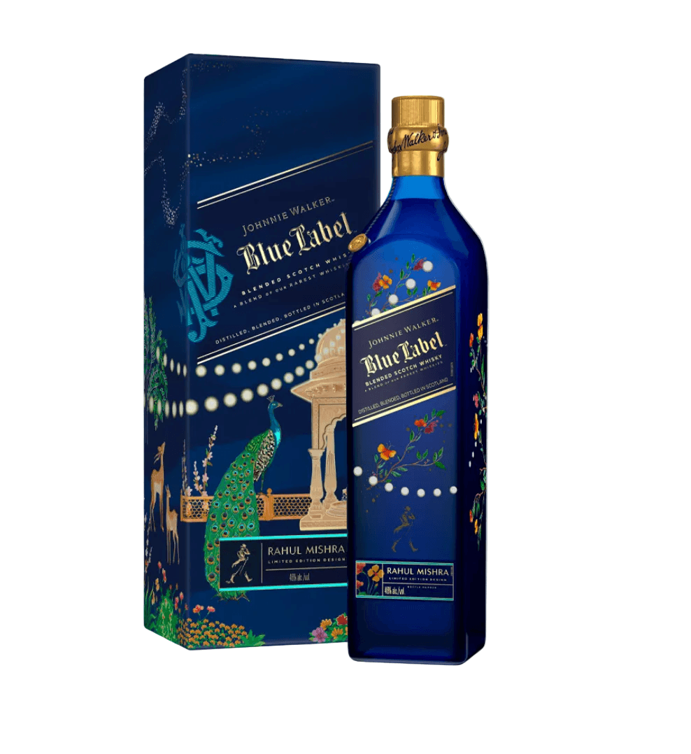 Deep blue gift box and matching blue glass bottle of Johnnie Walker Blue Label X Rahul Mishra Limited Edition Design blended Scotch whisky. The luxurious presentation features intricate Indian-inspired artwork: a vibrant peacock, deer, ornate architecture resembling an Indian palace, floral embroidery motifs, and delicate gold and white dotted patterns. 