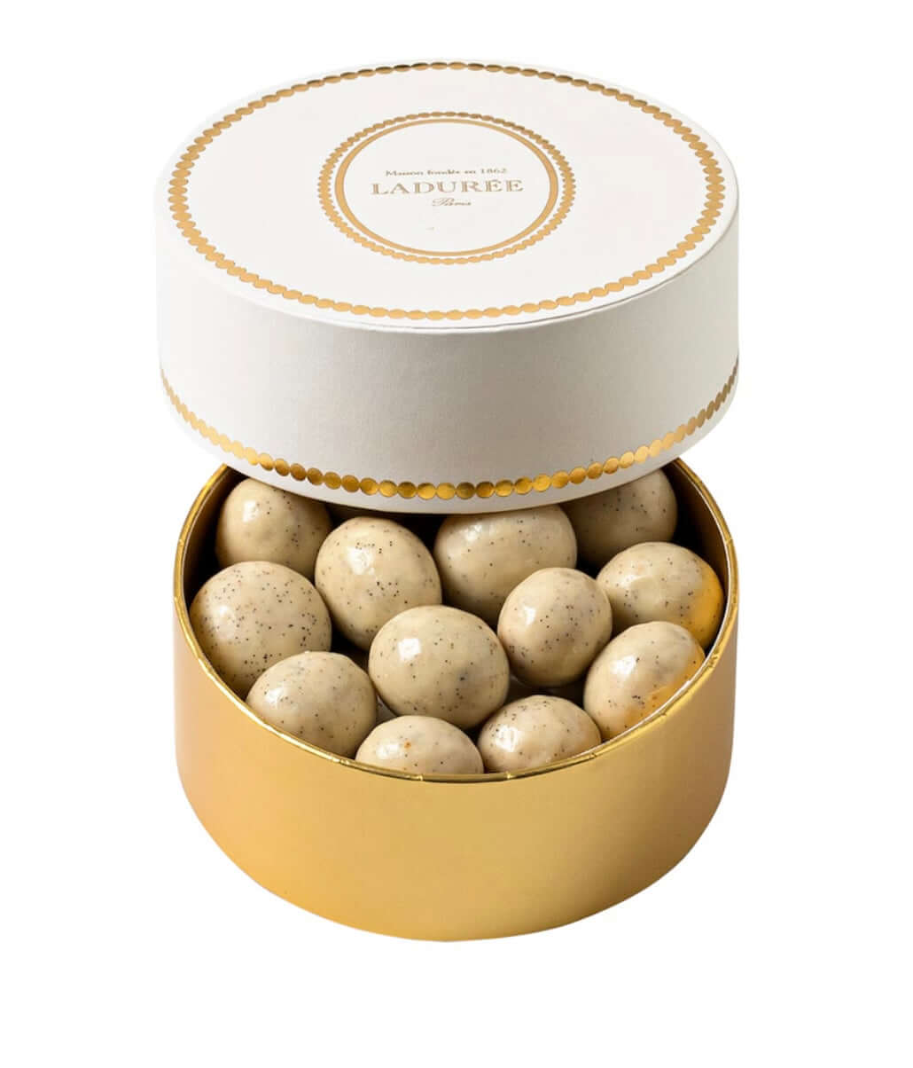 Round gold box with white lid containing round beige candies, branded 'Laduree'.