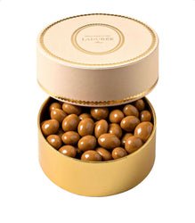 Round gold box with chocolate candies and 'Ladurèe' branding on a white background