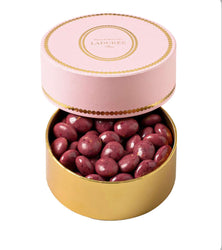 Round gold tin with pink lid containing purple candies, branded 'Ladurée'.