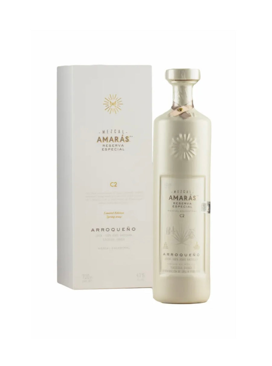 Cream-white bottle and matching white gift box of Mezcal Amarás Reserva Especial Arroqueño C2 (700ml), limited-edition Spring 2024 ancestral mezcal from wild Arroqueño agave, Oaxaca. Elegant frosted glass with embossed gold sunburst logo, gold metallic label text including "AMARÁS RESERVA ESPECIAL", "ARROQUEÑO", "C2", "Limited Edition Spring 2024", "Joven - 100% Agave Americana", "Ancestral Mezcal", "43% ALC/VOL", and "HECHO EN TUXTEPEC, OAXACA". Box features gold foil Amarás logo and text.