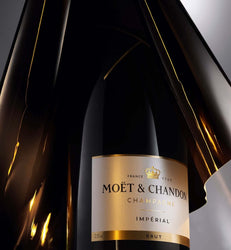 A close-up of a Moët & Chandon Impérial Brut champagne bottle with a reflective black glass body and a cream label with gold accents.