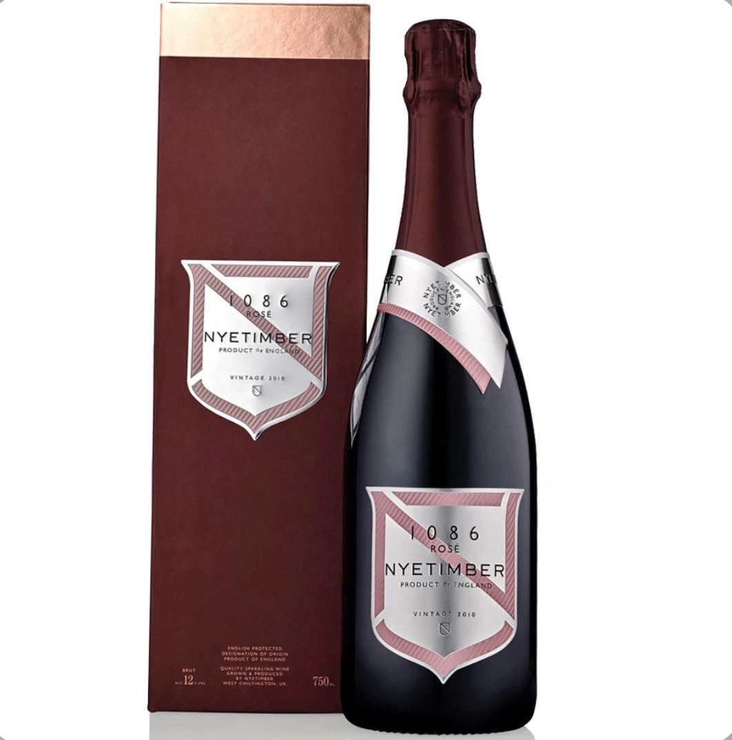 Burgundy gift box and deep burgundy bottle of Nyetimber 1086 Rosé Vintage 2010 English sparkling wine (75cl / 750ml). The tall rectangular gift box is matte burgundy with a copper-toned top band and a central silver-and-pink shield label featuring 