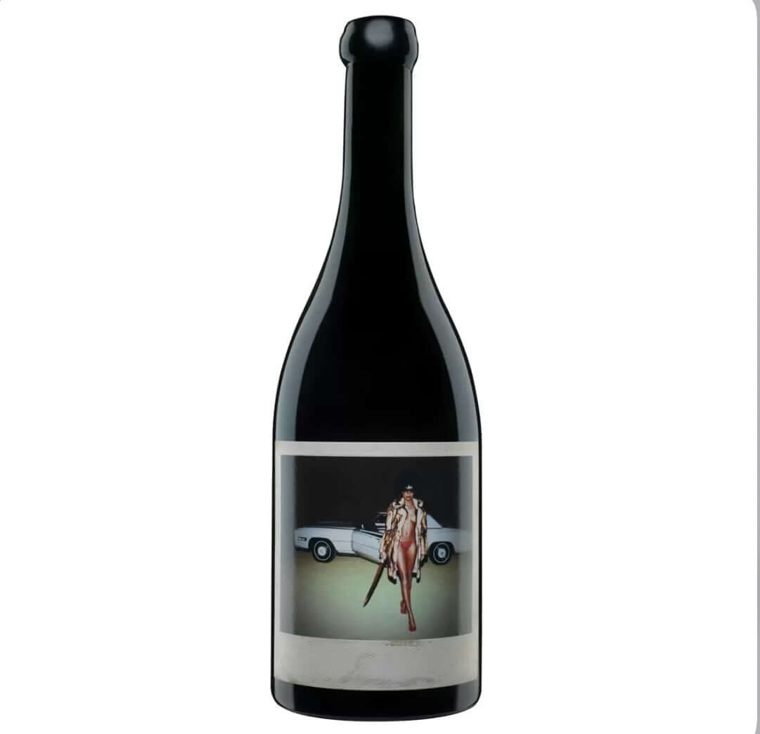 Dark black glass bottle of Orin Swift Machete California red wine (likely 2021 or similar vintage) with a striking, artistic label. The label features a bold, provocative photograph of a glamorous woman in a fur coat and red bikini, posing confidently next to a white convertible car, holding a large machete.