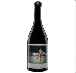Dark black glass bottle of Orin Swift Machete California red wine (likely 2021 or similar vintage) with a striking, artistic label. The label features a bold, provocative photograph of a glamorous woman in a fur coat and red bikini, posing confidently next to a white convertible car, holding a large machete.