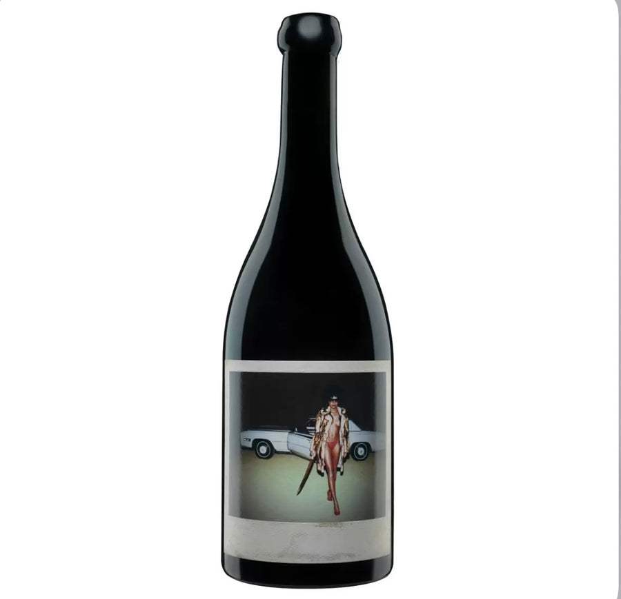 Dark black glass bottle of Orin Swift Machete California red wine (likely 2021 or similar vintage) with a striking, artistic label. The label features a bold, provocative photograph of a glamorous woman in a fur coat and red bikini, posing confidently next to a white convertible car, holding a large machete.