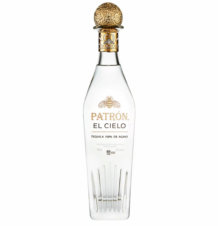 Clear glass bottle of Patrón El Cielo four-times distilled luxury blanco tequila with a distinctive tall, elegant shape featuring vertical etched lines at the base resembling agave leaves or crystal facets. The bottle contains crystal-clear liquid and has a prominent gold foil capsule with intricate embossed bee and floral motifs.