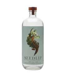A clear glass bottle of Seedlip Non-Alcoholic Spice 94 gin with a light blue-green label featuring a botanical illustration of a cinnamon stick and a brown cap, on a white background.