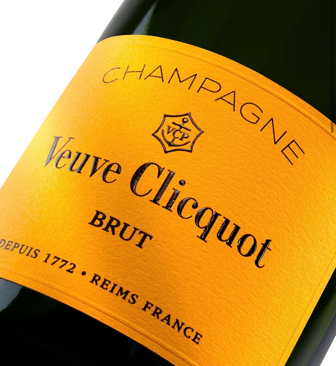 Close-up of a Veuve Clicquot Brut champagne bottle label, showing the brand name, 'Champagne', and 'BRUT' on a bright yellow-orange label against a dark bottle background.