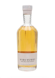 A bottle of Wire Works Single Malt English Whisky, featuring a clear glass bottle filled with golden amber whisky, a cream-colored label, and a white screw cap, set against a plain white background.