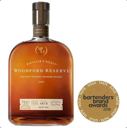 Amber glass bottle of Woodford Reserve Distiller's Select Kentucky Straight Bourbon Whiskey with a distinctive rounded, barrel-inspired shape and rich copper-amber liquid. The bottle features a dark gray foil capsule with embossed text, a prominent label with "WOODFORD RESERVE" in elegant uppercase gold lettering, "DISTILLER'S SELECT" arched above, and "KENTUCKY STRAIGHT BOURBON WHISKEY" below. 