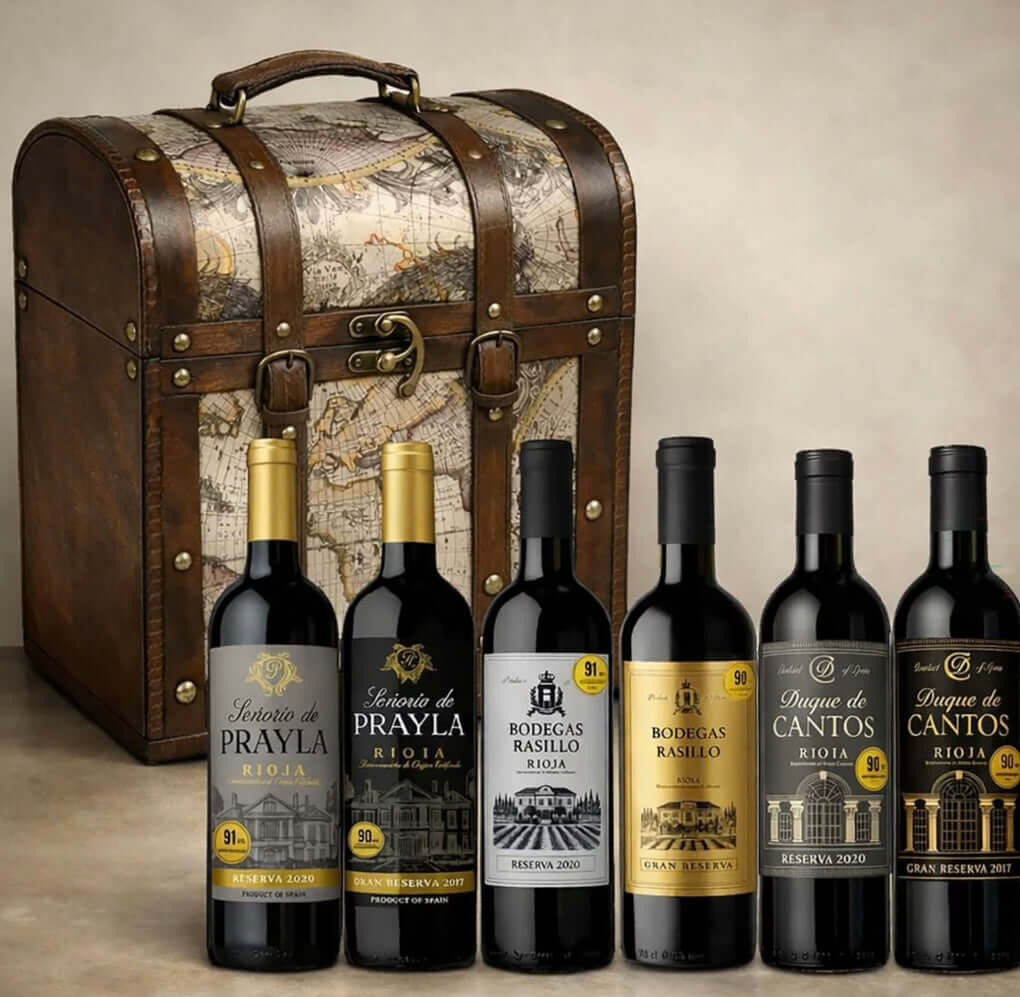 The Rioja Chest wine gift set: a domed wooden keepsake trunk with leather straps and antique map panels, with its six 75cl bottles standing in front — Señorío de Prayla Reserva 2020 and Gran Reserva 2017, Bodegas Rasillo Reserva 2020 and Gran Reserva, Duque de Cantos Reserva 2020 and Gran Reserva 2017