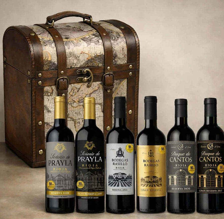 The Rioja Chest wine gift set: a domed wooden keepsake trunk with leather straps and antique map panels, with its six 75cl bottles standing in front — Señorío de Prayla Reserva 2020 and Gran Reserva 2017, Bodegas Rasillo Reserva 2020 and Gran Reserva, Duque de Cantos Reserva 2020 and Gran Reserva 2017