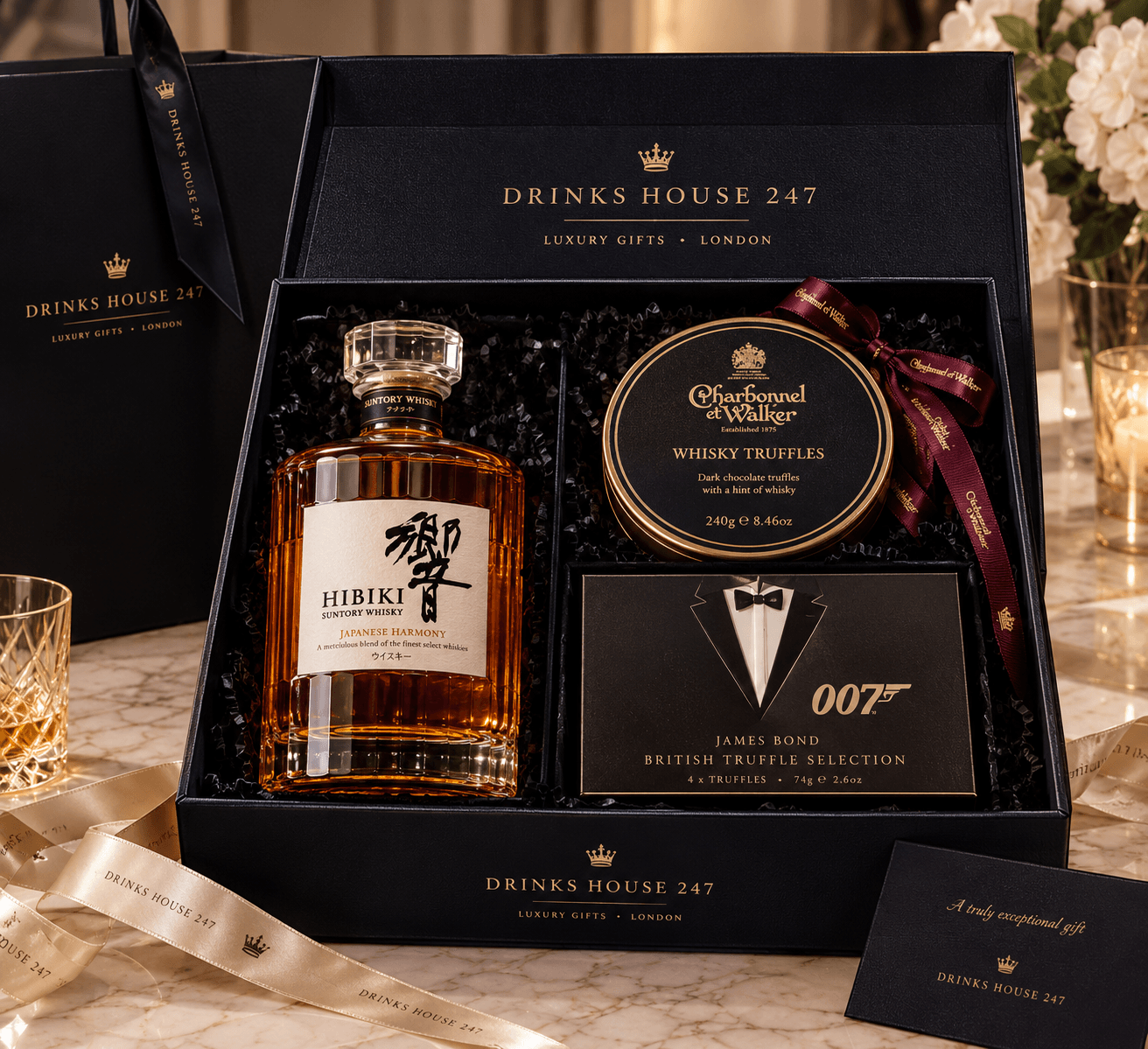 The Hibiki Harmony & Truffles Hamper in a black and gold Drinks House 247 gift box, holding Hibiki Japanese Harmony whisky 70cl, Charbonnel et Walker Whisky Truffles and the James Bond Tuxedo British Truffle Selection on shredded tissue, with a ribboned gift bag and message card
